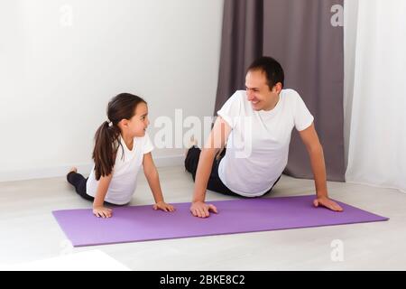 Schöner junger Vater und seine süße kleine Tochter tun Reverce Plank mit Bein heben auf dem Boden zu Hause. Fitness-Workout für die ganze Familie. Stockfoto