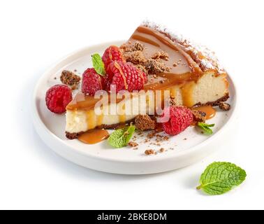 Stück Karamellkäsekuchen mit frischen Himbeeren und Minzblättern auf weißem Teller Stockfoto