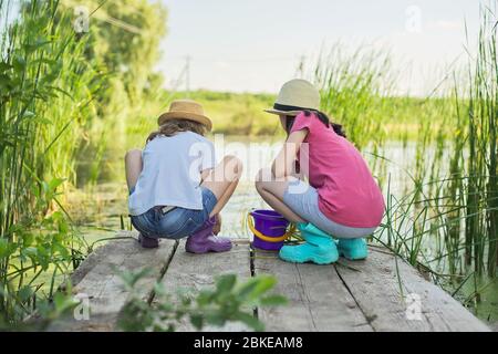 Mädchen sitzen auf Holzpier und fangen Wasserschnecken im Eimer Stockfoto