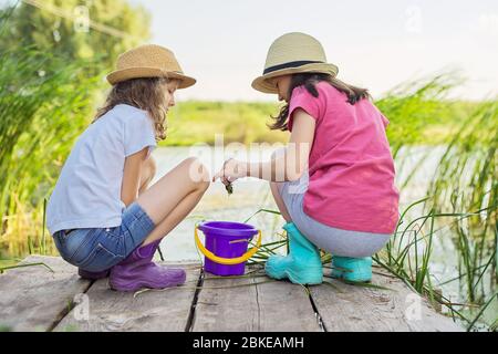 Mädchen sitzen auf Holzpier und fangen Wasserschnecken im Eimer Stockfoto