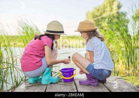 Mädchen sitzen auf Holzpier und fangen Wasserschnecken im Eimer Stockfoto