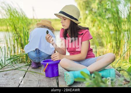 Mädchen sitzen auf Holzpier und fangen Wasserschnecken im Eimer Stockfoto