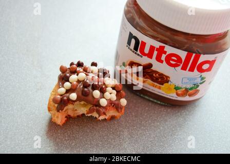 Nahaufnahme eines gebissenen hausgemachten Muffins mit Schokoladenüberzug und einem Glas Nutella daneben Stockfoto