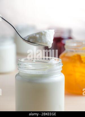 Hausgemachter Joghurt mit Orangenmarmelade Löffel essen aus einem Glas auf einem weißen Holztisch. Gesundes Milchviehfrühstück. Stockfoto