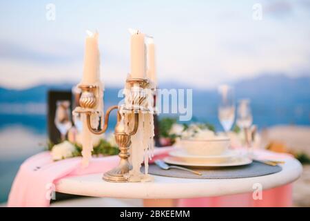 Nahaufnahme eines Hochzeitstisch am Empfang. Brennende Kerzen im Kandelaber auf dem Tisch mit dem rosa Tuch und den cremefarbenen Tellern auf dem Hintergrund a Stockfoto