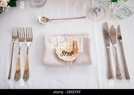 Nahaufnahme eines Hochzeitstisch. Die Aufschrift BRÄUTIGAM auf der Schale in der Mitte des Tisches. Die Bedienung des Tisches - die Messer, die Gabeln, die Gläser, die Weingläser Stockfoto