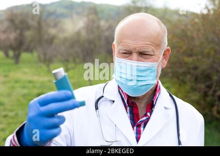 Älterer männlicher Arzt mit chirurgischer Maske, die einen Asthma-Inhalator im Freien hält Stockfoto