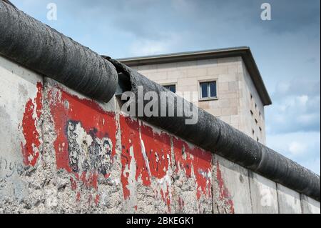 Überreste der Berliner Mauer, Berlin, Deutschland. Buntes Bild mit rotem Farbspritzer auf einer grauen Wand und dunklem, bewölktem Himmel Hintergrund. Stockfoto