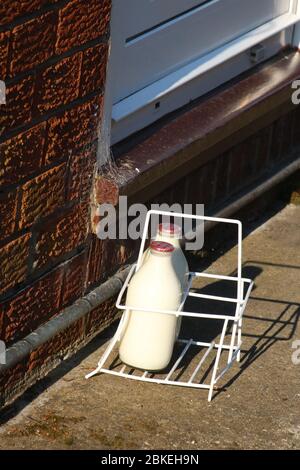 Milchkiste auf der Auffahrt vor der Haustür mit Hausmilch-Lieferung, zwei Pints halbentrahmte Milch in wiederverwendbaren Glasflaschen. Stockfoto