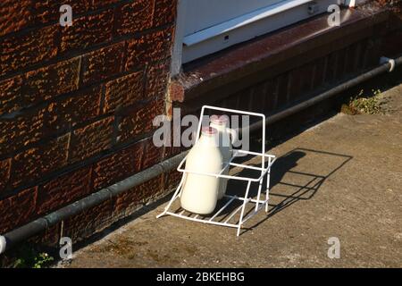 Milchkiste auf der Auffahrt vor der Haustür mit Hausmilch-Lieferung, zwei Pints halbentrahmte Milch in wiederverwendbaren Glasflaschen. Stockfoto