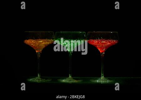 Drei cocktailgläser im martini-Stil mit beleuchtetem Display und hellem Wasserkaviar im Cocktailstil. Glaswaren Kunst mit farbigem Wasser Stockfoto