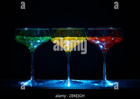 Drei cocktailgläser im martini-Stil mit beleuchtetem Display und hellem Wasserkaviar im Cocktailstil. Glaswaren Kunst mit farbigem Wasser Stockfoto