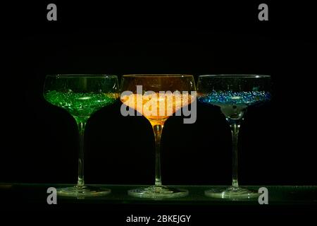 Drei cocktailgläser im martini-Stil mit beleuchtetem Display und hellem Wasserkaviar im Cocktailstil. Glaswaren Kunst mit farbigem Wasser Stockfoto