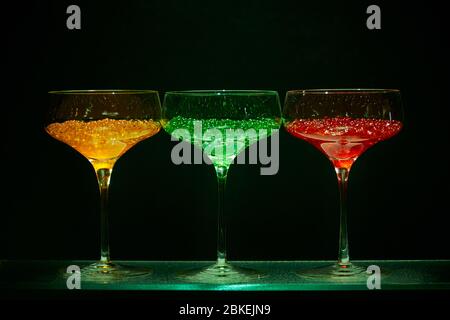 Drei cocktailgläser im martini-Stil mit beleuchtetem Display und hellem Wasserkaviar im Cocktailstil. Glaswaren Kunst mit farbigem Wasser Stockfoto
