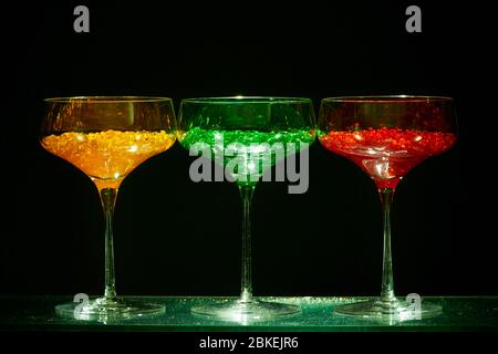 Drei cocktailgläser im martini-Stil mit beleuchtetem Display und hellem Wasserkaviar im Cocktailstil. Glaswaren Kunst mit farbigem Wasser Stockfoto
