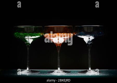 Drei cocktailgläser im martini-Stil mit beleuchtetem Display und hellem Wasserkaviar im Cocktailstil. Glaswaren Kunst mit farbigem Wasser Stockfoto