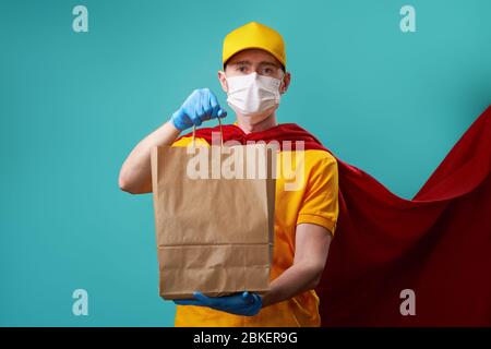 Kurier mit Tasche trägt medizinische Gesichtsmaske in Superhelden Mantel. Konzept der Superheldentum Kurier während Coronavirus Ausbruch. Stockfoto