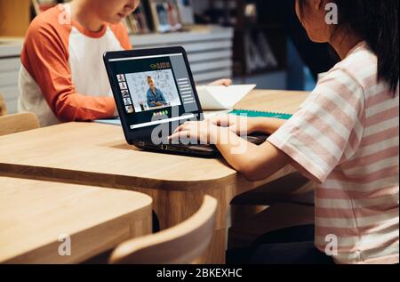Asiatische Schüler Videokonferenz mit Lehrer und Freunde mit E-Learning-App auf Laptop-Computer zu Hause.Frau auf Teppich liegend.New normales Lernen Stockfoto