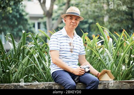 Porträt des positiven Senior Asian Mann ruht im Park mit Tablet-Computer und Digitalkamera Stockfoto