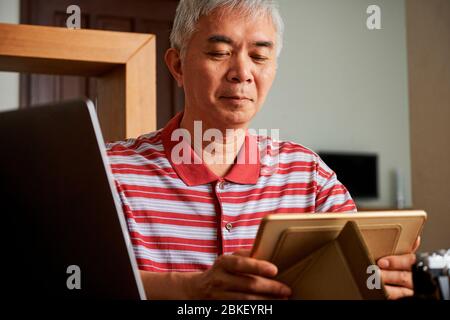 Älterer Chinese, der während der Quarantäne von zu Hause aus arbeitet, stellt Tablet-Computer auf Tablet-Ständer Stockfoto