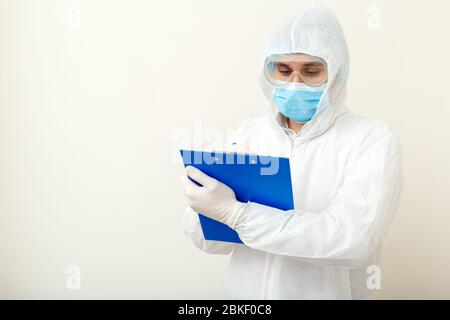 Coronavirus, Covid-19 Arztbesuch. Arzt in schützenden medizinischen Anzug, biologische Gefahr, Gesichtsmaske Arzt schreibt auf Tablet. Medizinische Versorgung Stockfoto