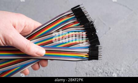 Steckverbindern der Überbrückungskabel. Regenbogen Drähte in der Hand auf isolierten Betonhintergrund. Farbige Kabel für elektronische Schaltung Stockfoto