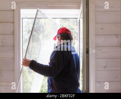 Arbeiter installieren Moskitonetz oder Moskitonetz-Bildschirm auf Holzfenster. Stockfoto