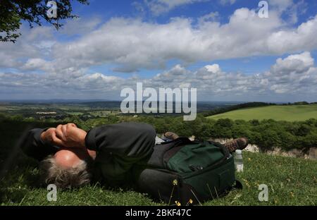 Mann, der sich im Sommersonne entspannt, unter einem Sommerhimmel liegt und seine Augen mit beiden Armen vor der Sonne schützt Stockfoto