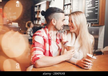 Glückliches junges Paar, schöner Kerl, charmantes Mädchen breites Lächeln, schauen mit liebevollen Augen, trinken Kaffee ihrer Pappbecher im Café, Blendung und Überbelichtung fo Stockfoto