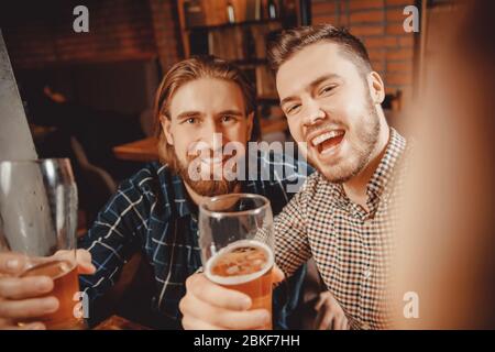 Selfie-Zeit. Zwei bärtige Hipster Freunde entspannen Bar, fotografieren am Telefon, trinken Bier und lächeln weit. Sie haben Spaß. Foto für Erinnerung im sozialen Netz Stockfoto