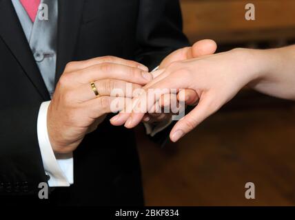 Goldring auf der Hand des Bräutigams, der der Braut einen weiteren Ring aufsetzt, Stockfoto