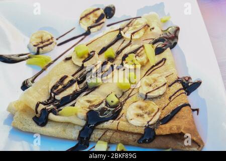 Traditionelle Dreiecke gefaltet Pfannkuchen mit Schokoladensauce und Obst Toppings während Street Food Festival. Serviert auf einem weißen Teller Stockfoto