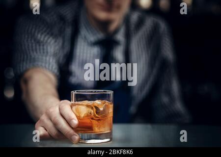 Barman hält Glas Whisky mit Eis für männliche Besucher aus. Konzeptruhe in der Bar. Stockfoto