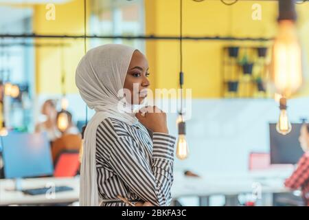 Trait einer schwarzen (afroamerikanischen) weiblichen muslimin, die in einem modernen Geschäftsbüro steht, während sie einen Hijab trägt. Stockfoto