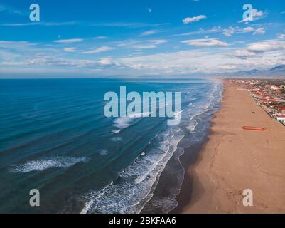 Meer breiten Sandstrand, blau klares Wasser spiegelt Himmel, Schäume, Glares in der Sonne am Sommertag. Kleine Häuser mit roten Dächern Entfernung. Draufsicht. Konzept von l Stockfoto