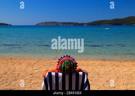 Ein Mann in einem lustigen panama sitzt in einem Liegestuhl an einem sauberen ökologischen Strand unter der Blauen Flagge in Kroatien. Sommer Urlaub am Meer am Meer Wasser, Reisen Stockfoto