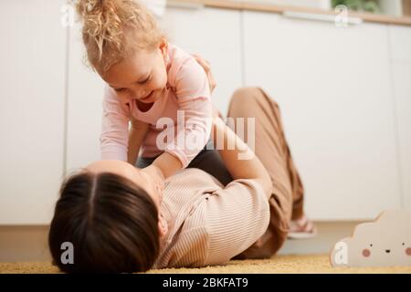 Junge Frau auf dem Boden liegend Spaß mit ihrer kleinen Tochter spielen, horizontal erschossen Stockfoto