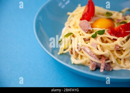 Carbonara Pasta - Spaghetti mit kleinen Stücken Speck, gemischt mit Sauce von Eiern, Parmesan-Käse. Blaue Platte auf blauem Hintergrund. Macanons mit Ei Stockfoto