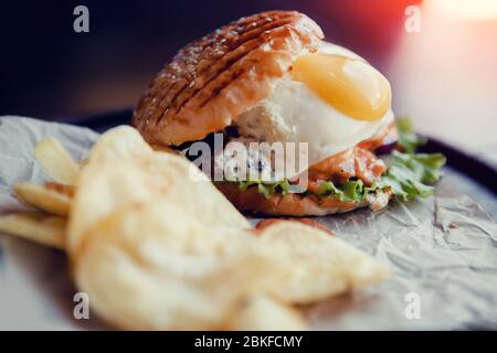 Burger mit Spiegelei, Fleischpastete, gegrilltem Brötchen. In der Nähe von Kartoffelchips. Konzept Fast Food Stockfoto