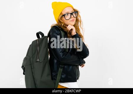 Europäische attraktive Mädchen in einem gelben Hut, Brille und einer Lederjacke mit einem Rucksack auf dem Rücken auf einem weißen Hintergrund mit Copyspace gekleidet. Stockfoto