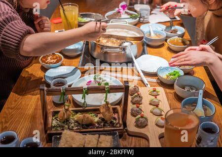 Tisch voller Gerichte und Zutaten, die im Hotpot-Restaurant mit drei Gästen zubereitet werden Stockfoto