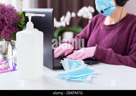 Alkohol Desinfektionsmittel Gel Handhygiene, medizinische chirurgische blaue Gesichtsmasken. Covid-19 Coronavirus. Frau arbeitet online von zu Hause aus auf Laptop.Remote-Arbeit.Video c Stockfoto