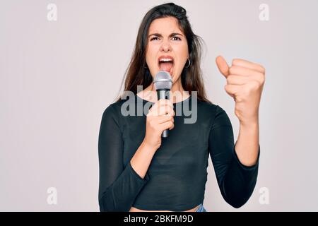 Junge schöne Sängerin Performerin Mädchen singen mit Musikmikrofon über isolierten Hintergrund verärgert und frustriert schreien vor Wut, verrückt und ye Stockfoto