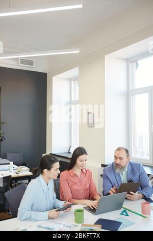 Gruppe von drei Geschäftsleuten sitzen am Tisch im modernen Büro Coworking auf neue Strategie, vertikale Schuss Stockfoto