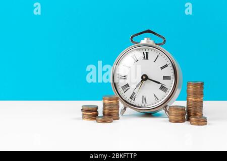 Wecker und Geldmünzen auf dem Tisch. Stockfoto