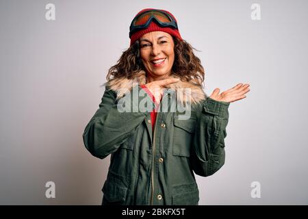 Mittlere Alter Skifahrer Frau im Schnee Sportbekleidung und Skibrille auf weißem Hintergrund erstaunt und lächelnd auf die Kamera während der Präsentation mit Hand und p Stockfoto