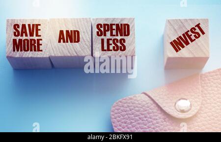 Mehr sparen und weniger ausgeben Investieren Sie auf Holzwürfel und rosa Ledertasche. Finanzkonzept Investitionen und Geldeinsparungen Stockfoto