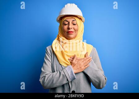 Mittelalter Brünette Architektin Frau mit muslimischen traditionellen Hijab und Sicherheitshelm lächelnd mit Händen auf der Brust mit geschlossenen Augen und dankbar ges Stockfoto