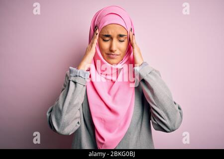 Junge, schöne Brunette-Geschäftsfrau mit pinkfarbenem muslimischem Hijab und Geschäftsjacke, die an Kopfschmerzen verzweifelt und gestresst ist, weil Schmerzen und m Stockfoto