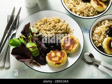 Ein einfaches veganes Mittag- oder Abendessen für eine Familie mit zwei Erwachsenen und einem Kind. Brauner Reis mit Soja-Okara und Kartoffelpasteten mit frischem Salat und Oliven auf einem m Stockfoto